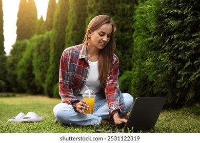 Woman with juice using laptop on green lawn in park - Powered by Shutterstock