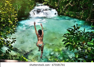 Woman jumping into amazing blue waterfall, in the middle of a forest