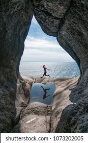 The Woman Jumping In The Pothole Over Background Of Blue Sea, Norway