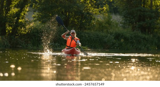 Woman kayaking in calm river waters at sunset, creating a splash with his paddle wearing an orange life jacket at summer. Kayak Water Sports concept image - Powered by Shutterstock