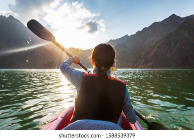Woman kayaking in a mountain surrounded lake at sunset - Powered by Shutterstock