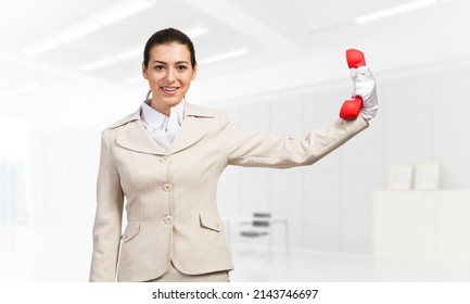 Woman Keep At Distance Vintage Red Phone. Elegant Operator In Business Suit Posing With Telephone In Light Office Interior Hotline Telemarketing And Communication. Business Assistance And Support