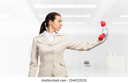 Woman Keep At Distance Vintage Red Phone. Elegant Operator In Business Suit Posing With Telephone In Light Office Interior Hotline Telemarketing And Communication. Business Assistance And Support