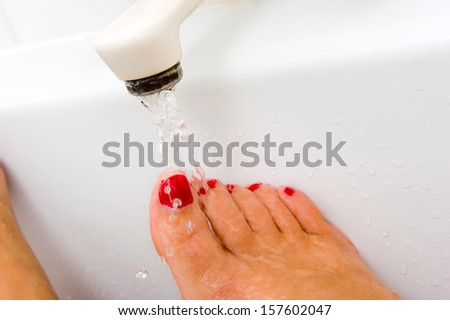 A woman is keeping her foot under the hot water of a bath faucet