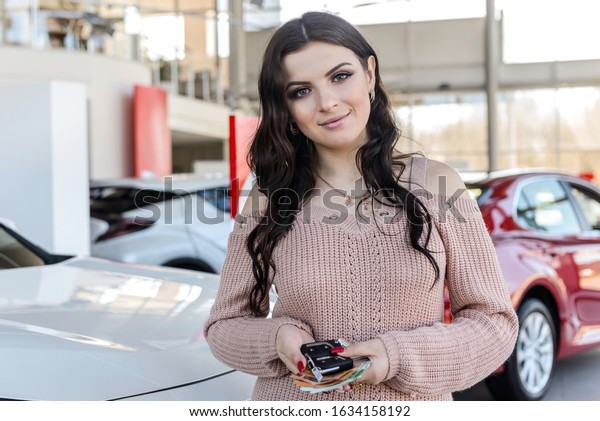 Woman\
with keys and euro banknotes standing near new\
car