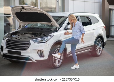 Woman Kicking Tire Of Car Standing With Hood Open