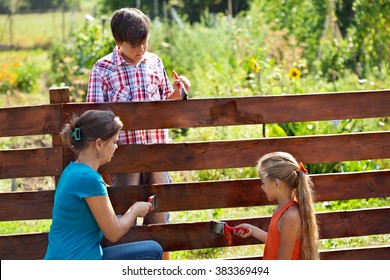 Woman And Kids Painting The Vegetables Garden Fence In Summer