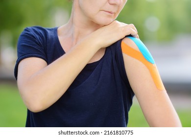 Woman With Kinesio Tape On Her Shoulder. Method Is Purported To Ease Pain And Disability From Athletic Injuries And A Variety Of Other Physical Disorders. Kinesiology, Physical Therapy, Rehabilitation