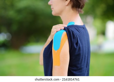 Woman With Kinesio Tape On Her Shoulder. Method Is Purported To Ease Pain And Disability From Athletic Injuries And A Variety Of Other Physical Disorders. Kinesiology, Physical Therapy, Rehabilitation