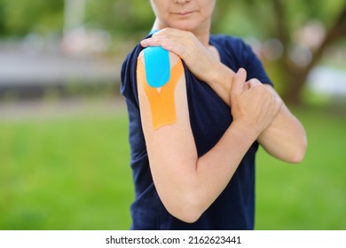 Woman With Kinesio Tape On Her Shoulder. Method Is Purported To Ease Pain And Disability From Athletic Injuries And A Variety Of Other Physical Disorders. Kinesiology, Physical Therapy, Rehabilitation