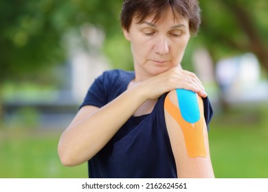 Woman With Kinesio Tape On Her Shoulder. Method Is Purported To Ease Pain And Disability From Athletic Injuries And A Variety Of Other Physical Disorders. Kinesiology, Physical Therapy, Rehabilitation