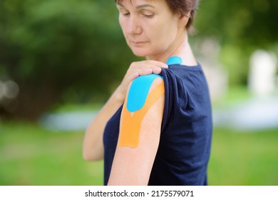 Woman With Kinesio Tape On Her Shoulder. Method Is Purported To Ease Pain And Disability From Athletic Injuries And A Variety Of Other Physical Disorders. Kinesiology, Physical Therapy, Rehabilitation