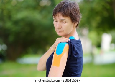 Woman With Kinesio Tape On Her Shoulder. Method Is Purported To Ease Pain And Disability From Athletic Injuries And A Variety Of Other Physical Disorders. Kinesiology, Physical Therapy, Rehabilitation