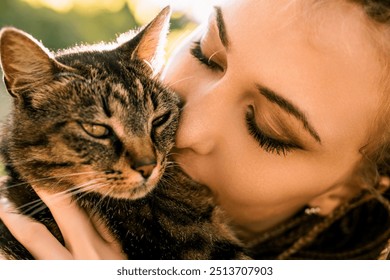 Woman kisses her tabby cat, showing love and affection in a cozy home bathed in warm sunlight - Powered by Shutterstock