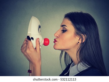 Woman kissing clown mask on gray wall background 