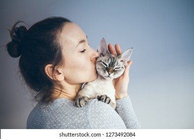Woman is kissing and cuddling her sweet and cute looking Devon Rex cat. Kitten feels happy to be with its owner.  Kitty sits in humans arms purrs.