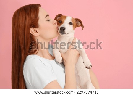 Woman kissing her cute Jack Russell Terrier dog on pink background. Space for text