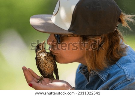 Woman kissing a little bird after being recovered from the ground when it fell from its nest.