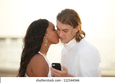 Woman Kissing The Man While He Looks At His Phone