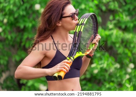 A woman kissing tennis rackets on a natural green background