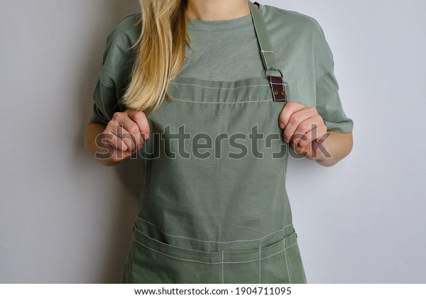A woman in a kitchen apron. Chef work in the\
cuisine. Cook in uniform, protection apparel. Job in food service.\
Professional culinary. Green fabric apron, casual clothing.\
Handsome baker posing