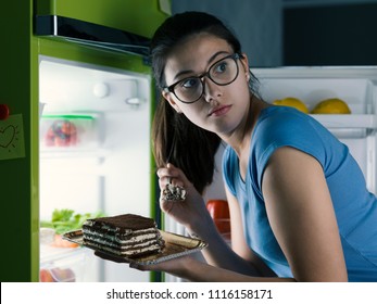 Woman In The Kitchen Having A Late Night Snack, She Is Taking A Delicious Dessert From The Fridge, Diet Fail Concept