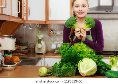 Woman In Kitchen With Many Green Leafy Vegetables, Fresh Produce On Counter. Young Housewife Holding Broccoli In Hand. Healthy Eating, Cooking, Vegetarian Food, Dieting And People Concept.