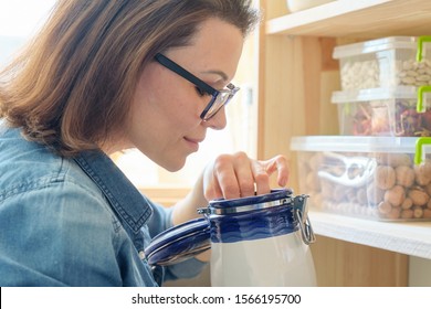 Woman In The Kitchen Near Wooden Rack With Cans For Storing Food.