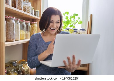 Woman In Kitchen Pantry With Stored Products, Holding Laptop