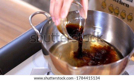 A woman in the kitchen putting soy sauce in a pot.