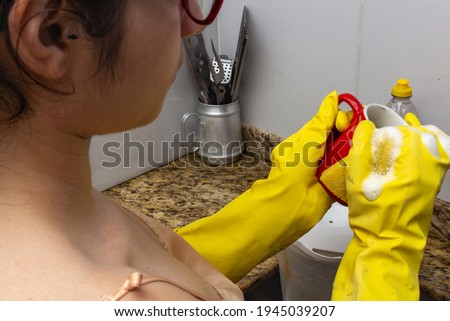 Woman in kitchen with yellow gloves washing red cup
