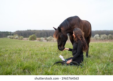 woman kneeling on the ground in her hand with a bow and a horse has her head near her