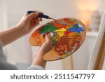 Woman with knife using palette near easel indoors, closeup