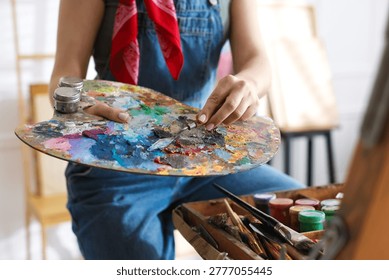 Woman with knife using palette while painting picture in studio, closeup