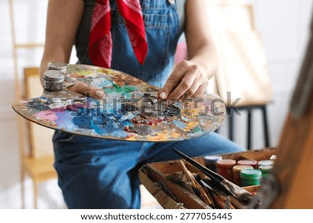 Woman with knife using palette while painting picture in studio, closeup