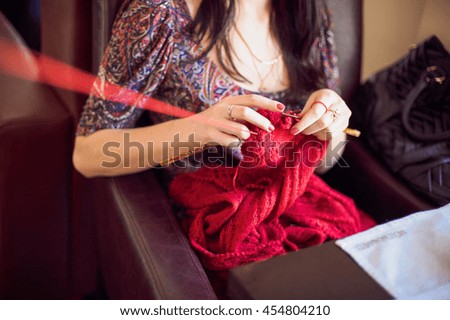 The woman knits a sweater red thread.