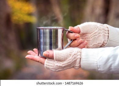 Woman With Knitted Fingerless Glove Is Holding Mug With Steaming Hot Drink. Refreshment During Hike In Nature. Hot Coffee Or Tea In Metal Cup