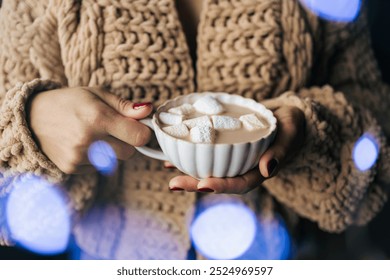 Woman in a knitted sweater holding a cup with coffee, hot chocolate, or cocoa drink with marshmallow. Close-up view. - Powered by Shutterstock