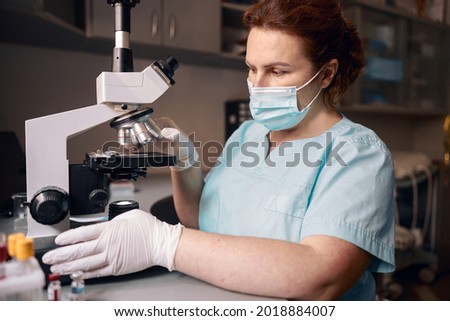 Woman lab assistant works with microscope to research material sample in clinic