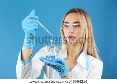 woman lab worker is holding laboratory flask and pipette on blue background, studio photo. biochemist conducts experiments close up, conceptual photo ストックフォト © 