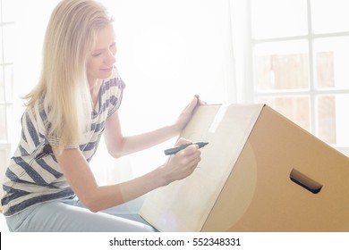 Woman Labeling Moving Box With Glass Material At Home