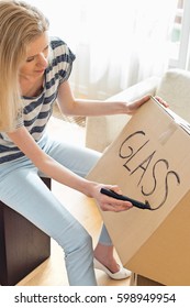 Woman Labeling Moving Box With Glass Material At Home