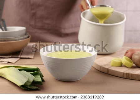 Woman with ladle pouring tasty leek soup at wooden table, focus on bowl