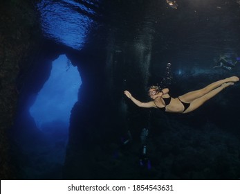 woman lady free diving apnea underwater cave sun beams and rays ocean scenery with human