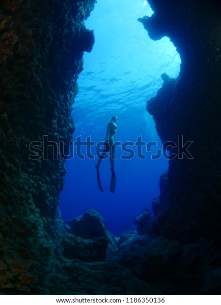 woman lady free diving apnea underwater in\
a cave cave with nice blue ocean\
scenery