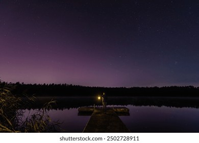 Woman with a lantern on a wooden pier, Aurora Borealis northern lights, Jupiter, Mars, stars over the forest lake in Latvia on August night. - Powered by Shutterstock