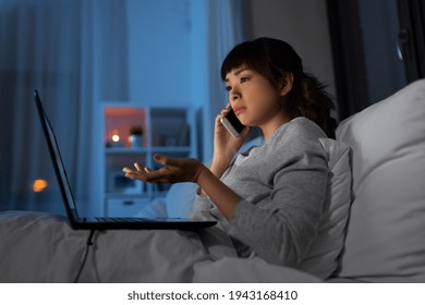 Woman With Laptop Calling On Phone In Bed At Night