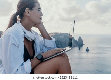 Woman, Laptop, Cliffside - Woman working on laptop while sitting on cliffside overlooking the ocean. - Powered by Shutterstock