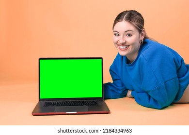 Woman With A Laptop. Greenscreen Laptop Mock Up. Laptop Template. Orange Background. 20-22 Years Old Caucasian Woman.