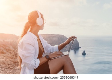 Woman Laptop Headphones Cliffside Ocean Sunset Digital Nomad Working Remotely - Powered by Shutterstock